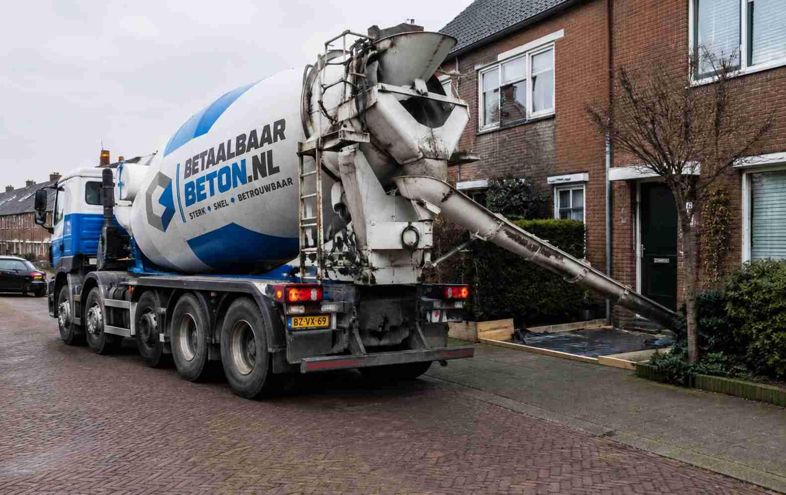 Betonmixer van BetaalbaarBeton.nl stort beton via een goot in een woonwijk